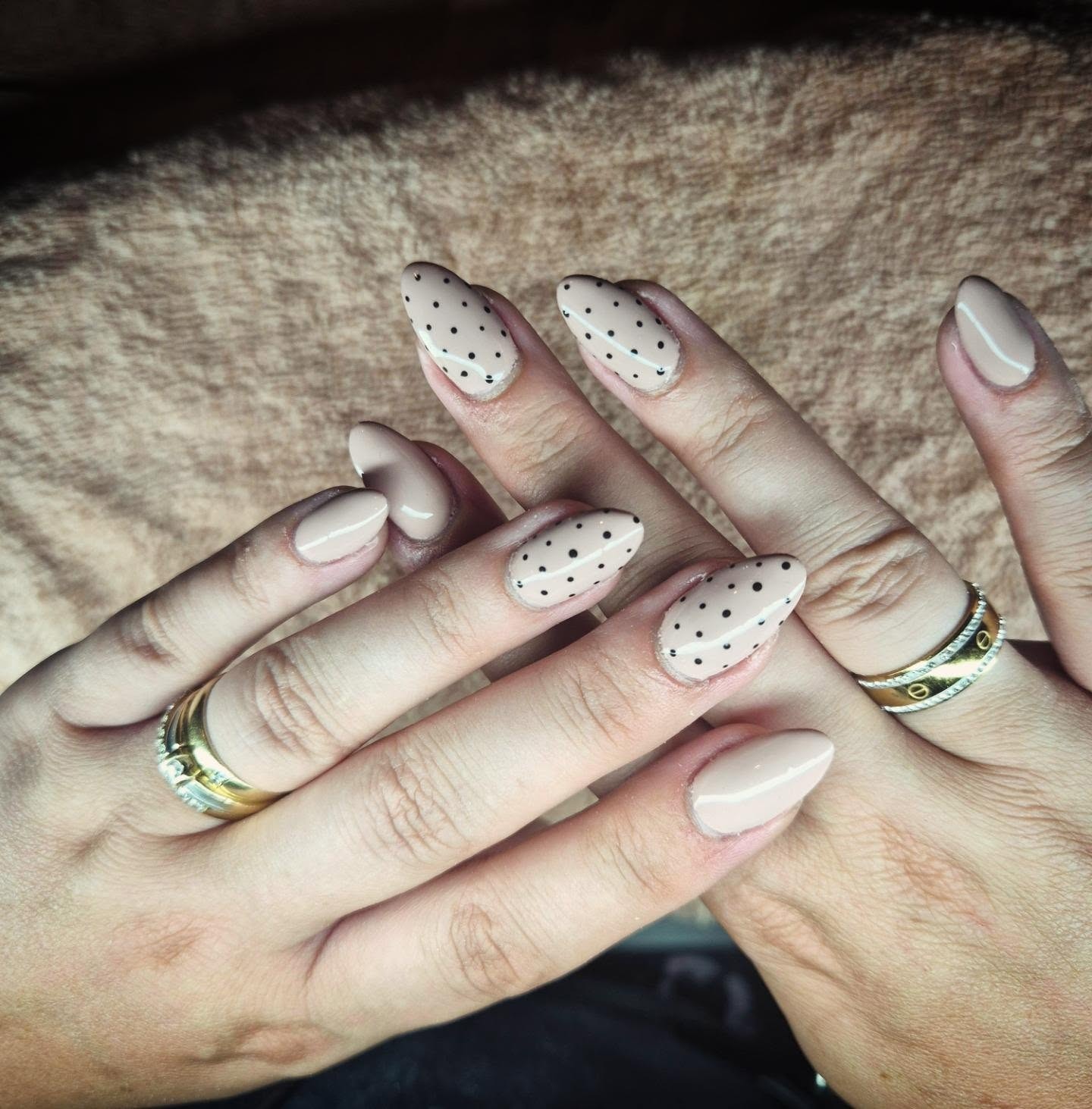 Handen met beige amandelnagels, vier ervan met zwarte stippen