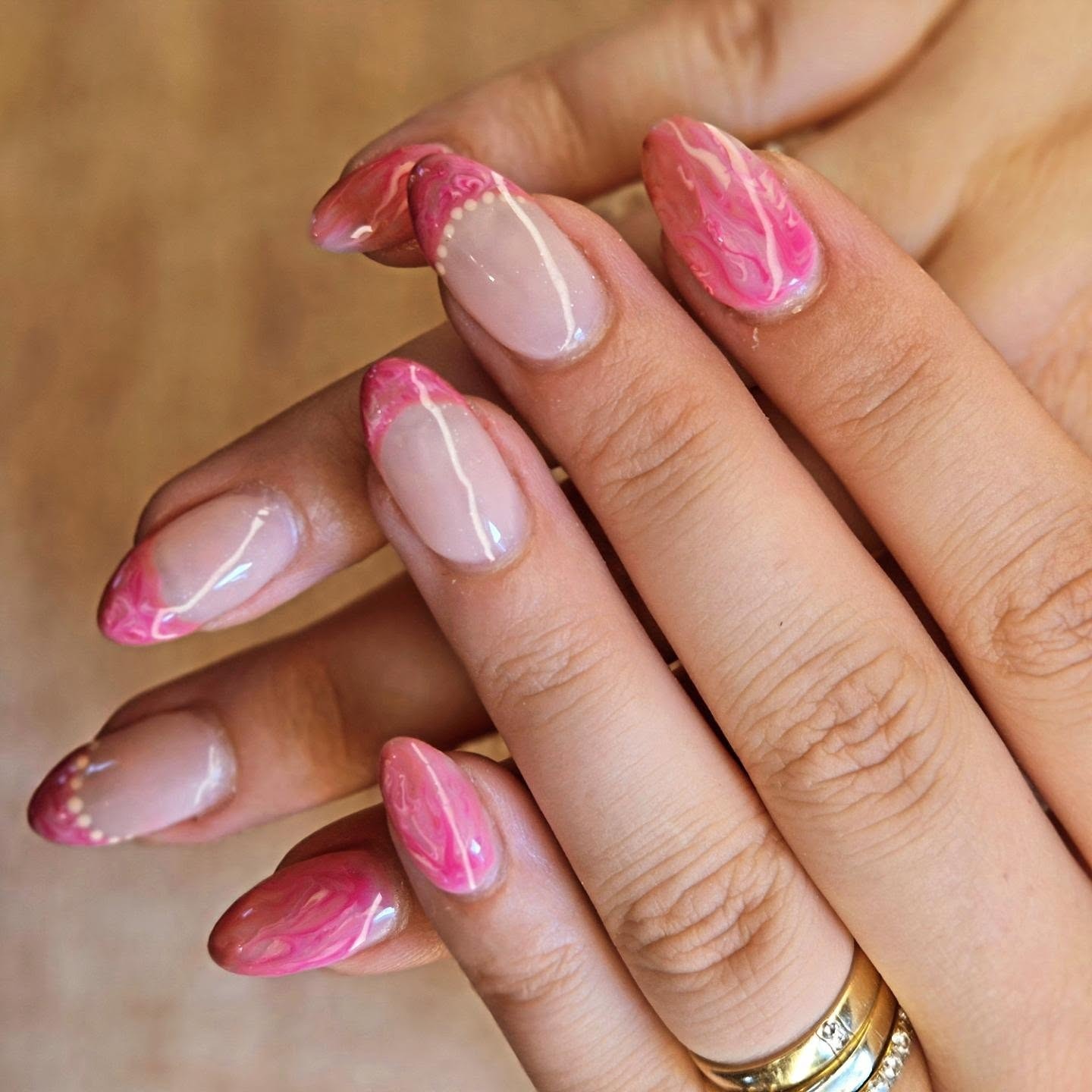 Amandelvormige nagels met roze marmer, een witte lijn en witte stipjes langs de rand