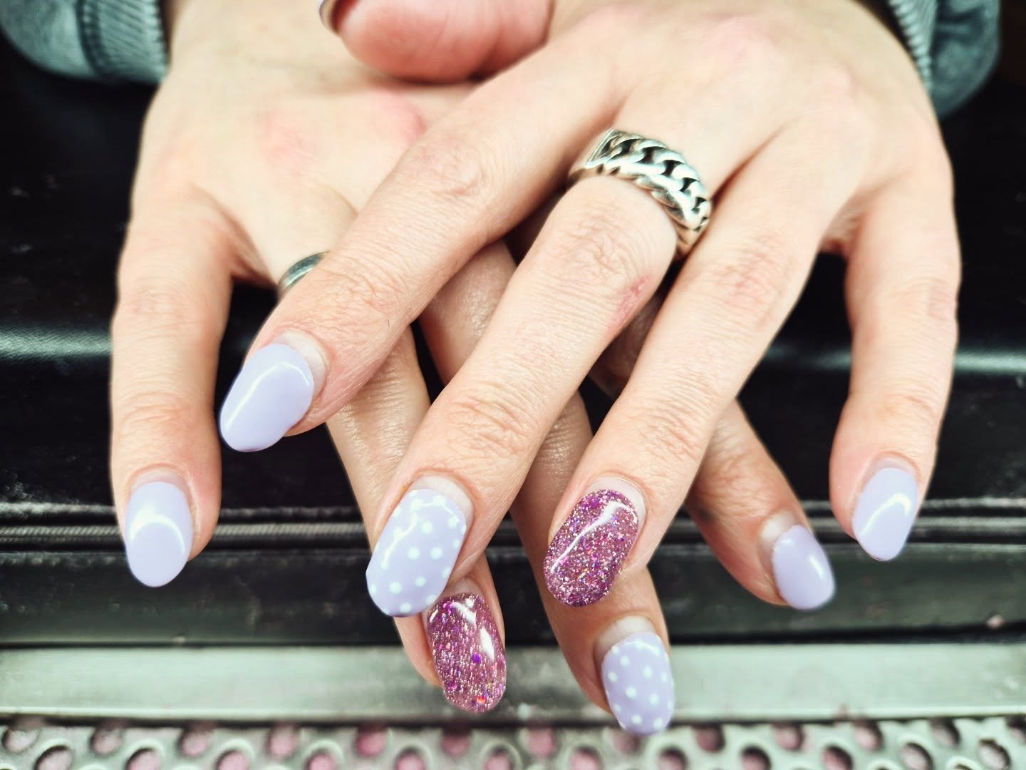 Twee handen met lila gelnagels, twee nagels met roze glitter en twee met witte stippen
